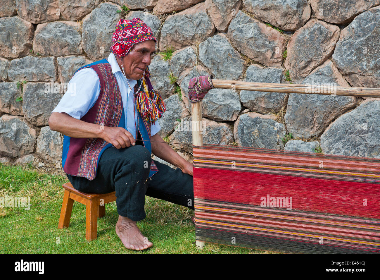 Älterer Mann mit einer Mütze, Quechua Indianer in traditioneller Kleidung, sitzen auf dem Boden auf der Bahre ein Webstuhl funktioniert Stockfoto