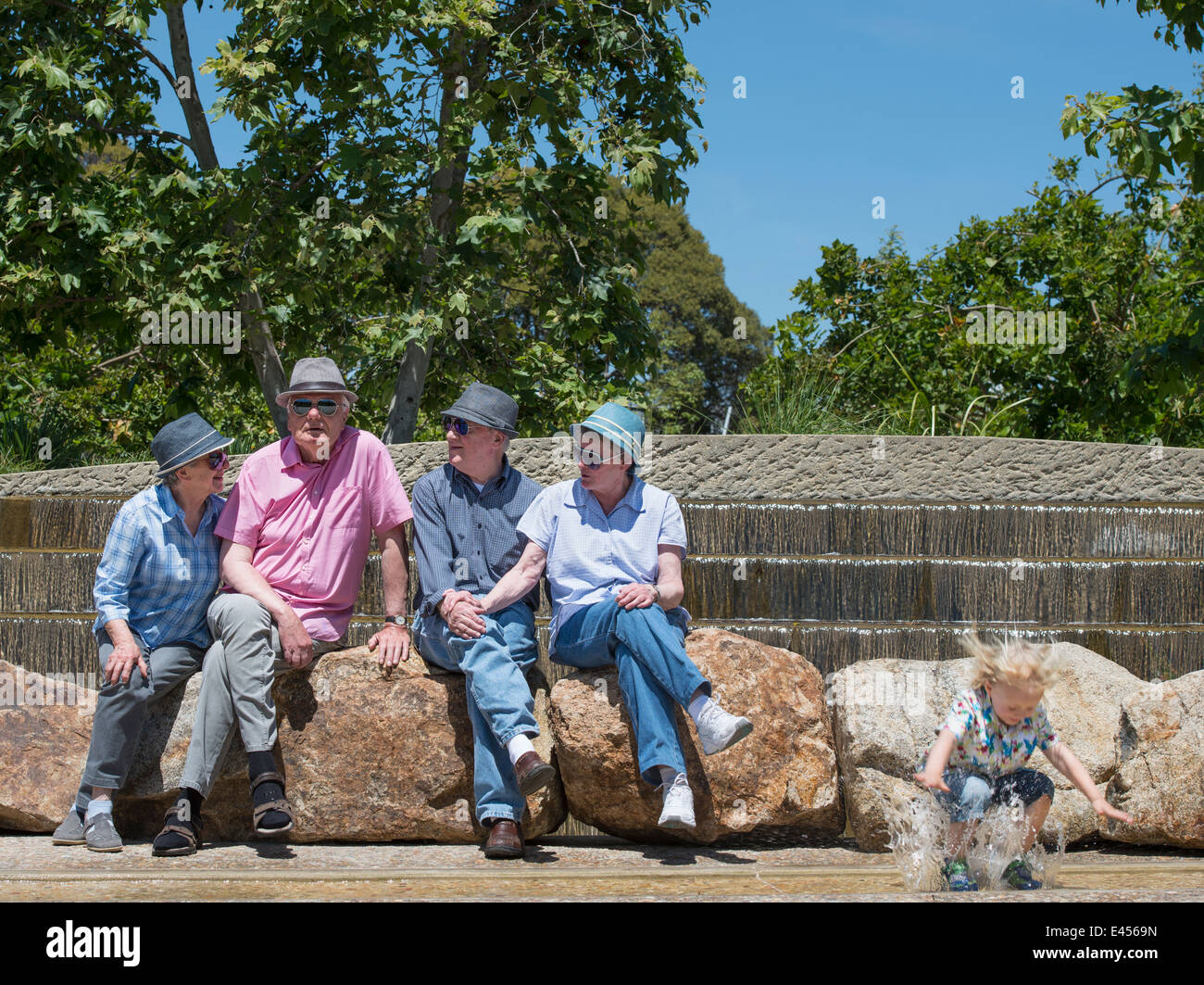 Großeltern sitzen im Park und Enkel planschen im Wasser Stockfoto