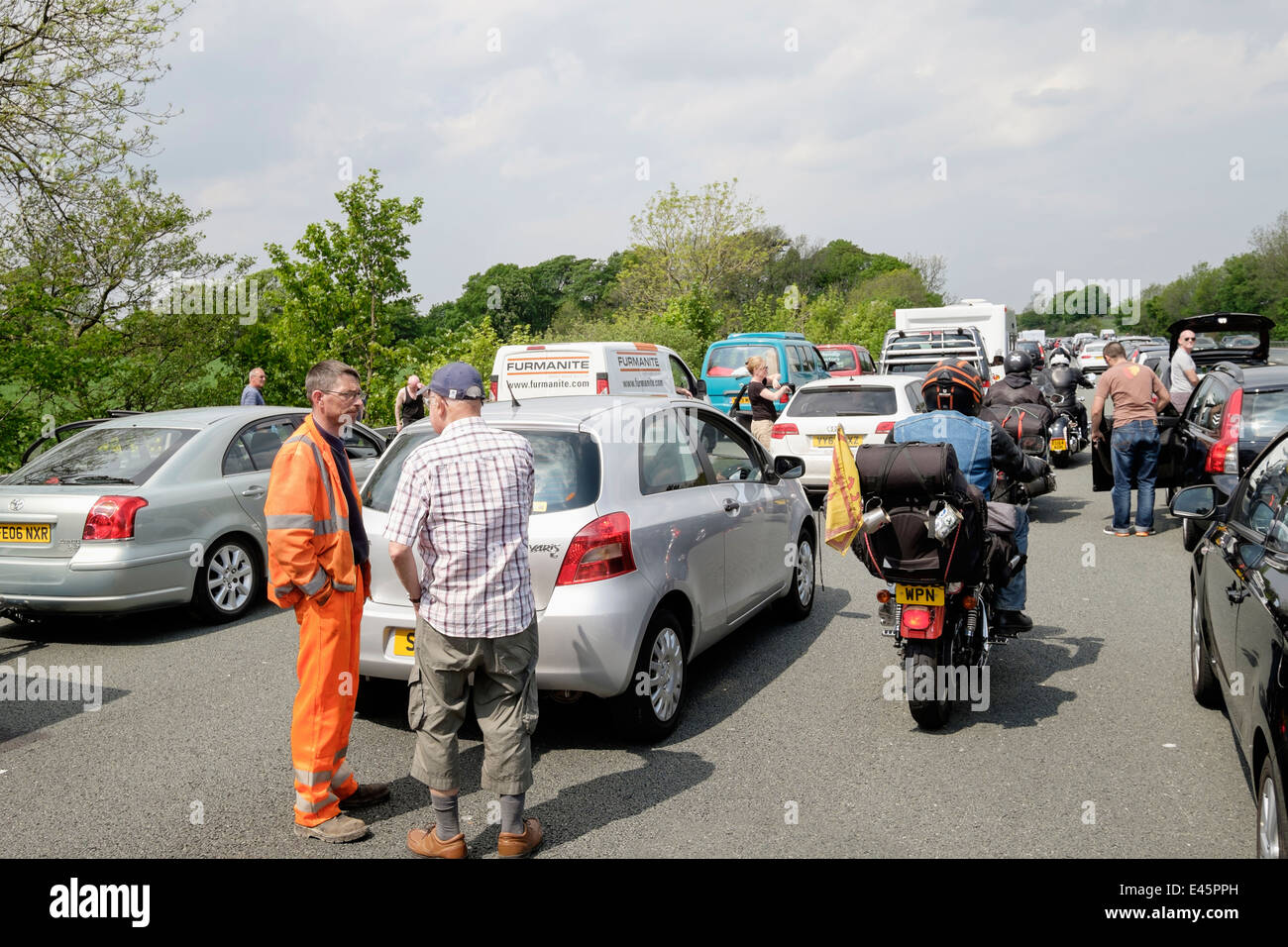 Motorräder fahren Reiten durch stehende Fahrzeuge im Stau mit Menschen stehen auf Fahrbahn auf der Autobahn M6. Lancashire England Großbritannien Stockfoto