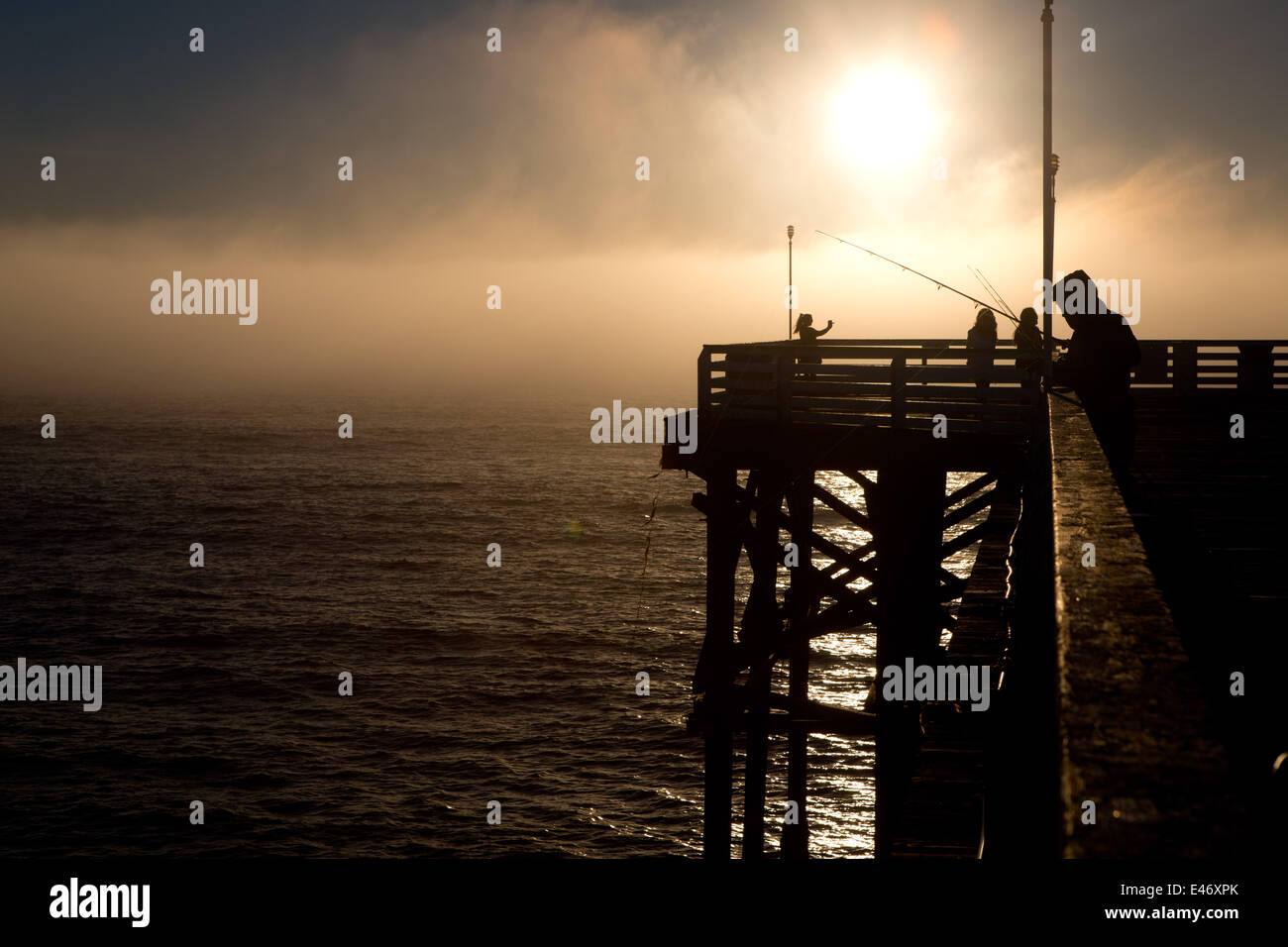Mann Angeln auf Crystal Pier, eine öffentliche Pier und Hotel, im Februar 2014. Am späten Nachmittag ist die Sonne eine Nebelbank aufschlussreich. Stockfoto