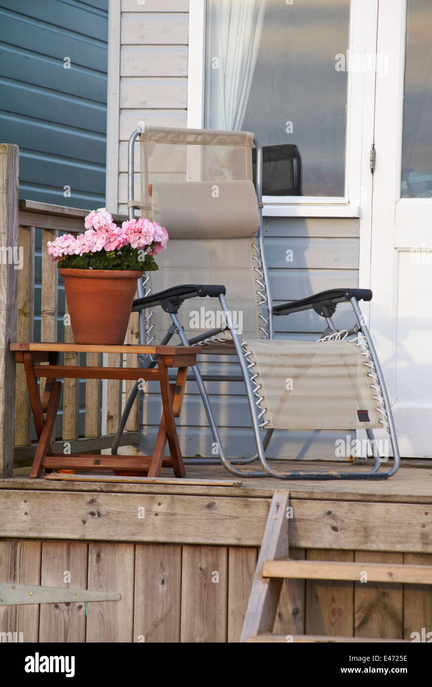 Liege und Topf mit Blumen auf dem Tisch auf der Terrasse der Strandhütte am Hengistbury Head im Juni Stockfoto