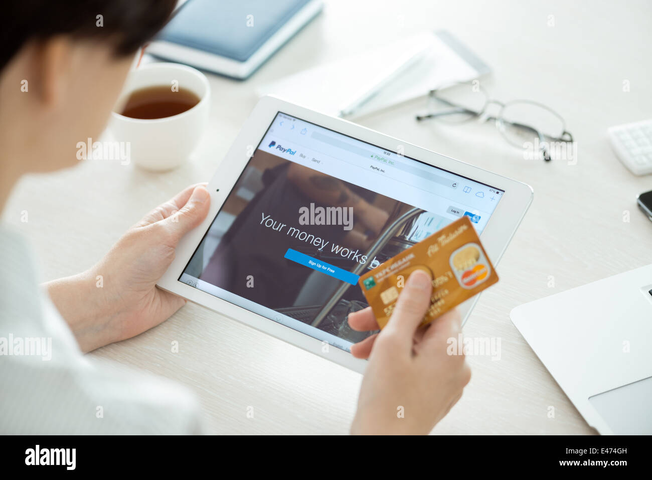 Person mit Mastercard Kreditkarte in der hand auf der Suche auf ein nagelneues Apple iPad Air mit Paypal-Website auf einem Bildschirm Stockfoto