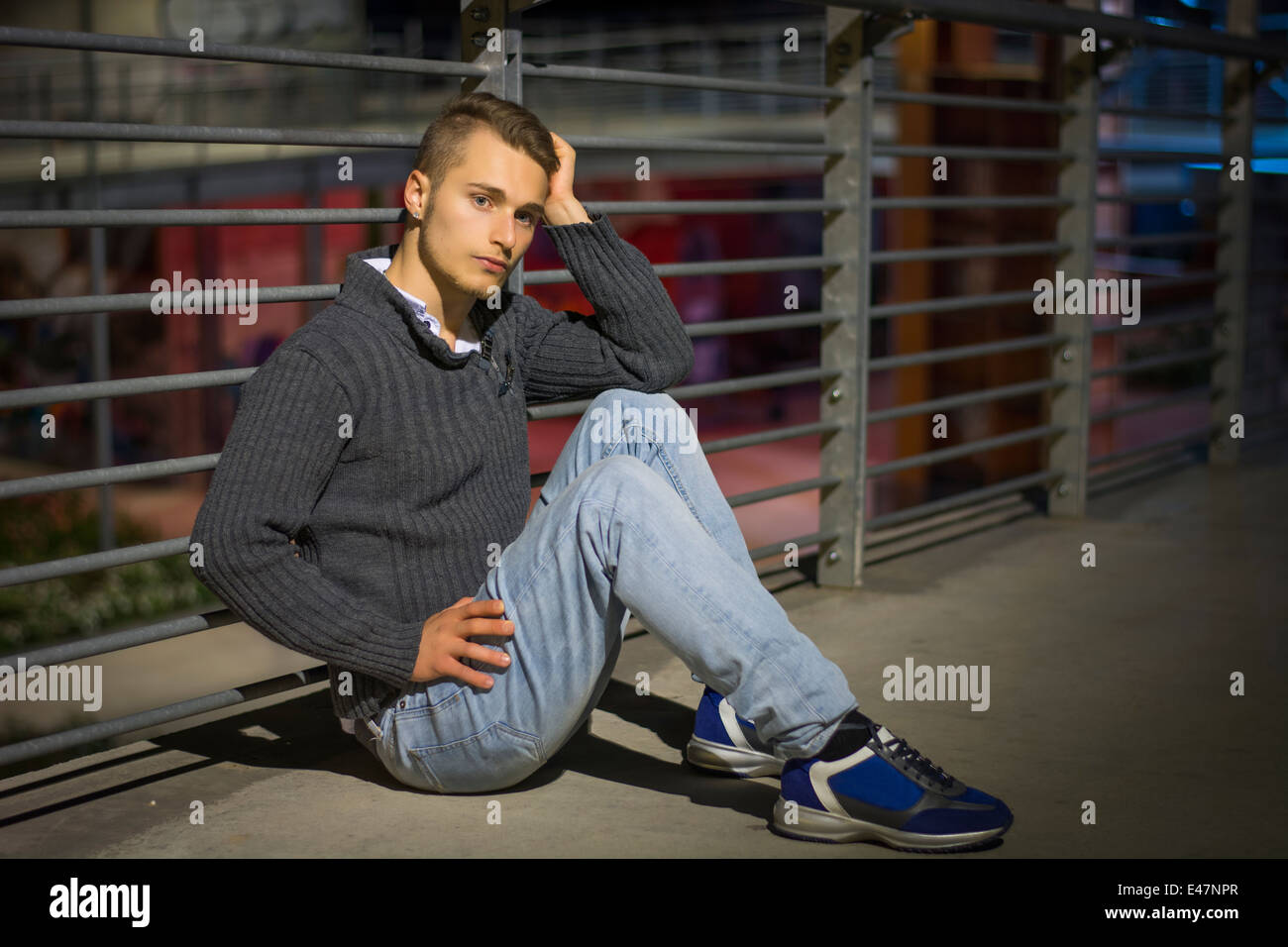 Hübscher blonder junger Mann sitzt allein in städtischen Umfeld, Blick in die Kamera, Nachtaufnahme Stockfoto