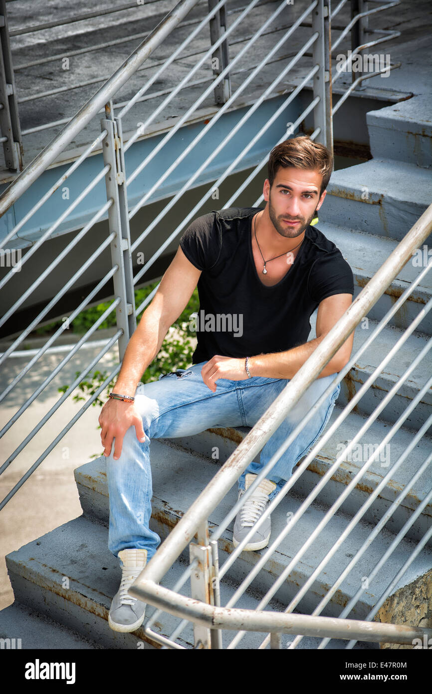 Handsome bärtiger jungen Mann sitzen im Freien in städtischer Umgebung Blick in die Kamera Stockfoto