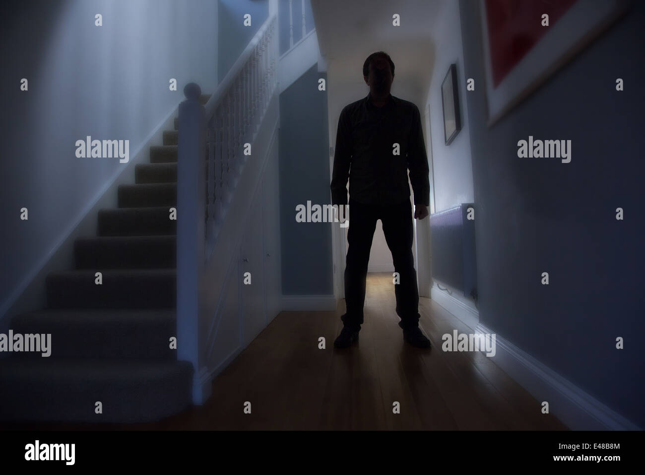 Silhouette eines Mannes stehend im Flur eines Hauses mit der Treppe zu seiner rechten. Stockfoto