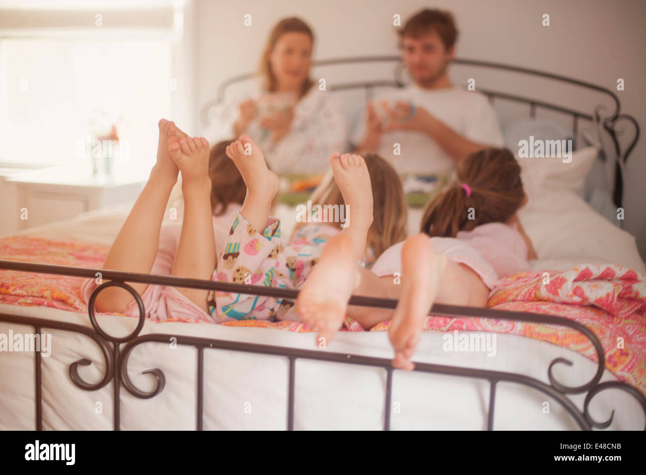Mädchen (4-5, 6 und 7) liegen im Bett der Eltern, während Mutter und Vater Frühstück Essen Stockfoto