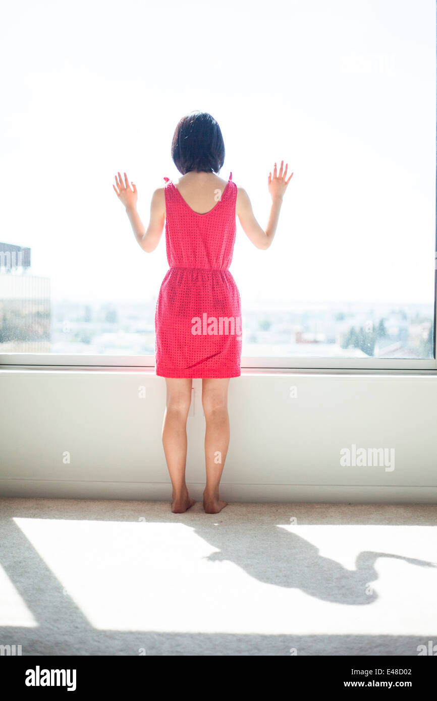 Rückansicht der jungen Frau stehen und blickte durch Fenster Stockfoto