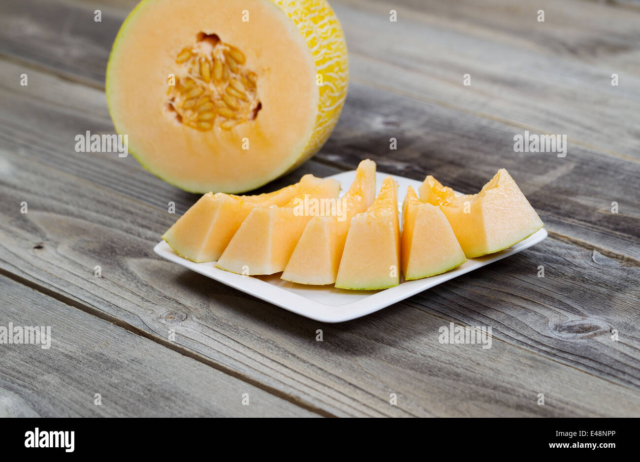 Detailansicht einer frisch geschnittenen Melone mit Scheiben auf weißen Teller und die Hälfte der Melone im Hintergrund auf rustikalen Holz Stockfoto