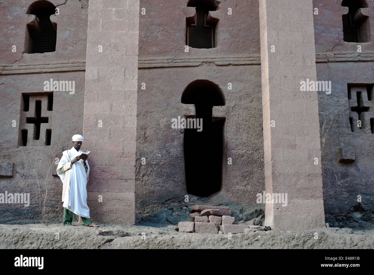Orthodoxer Priester, einem religiösen Buch vor einem Felsen gehauene Kirche (Äthiopien) Stockfoto