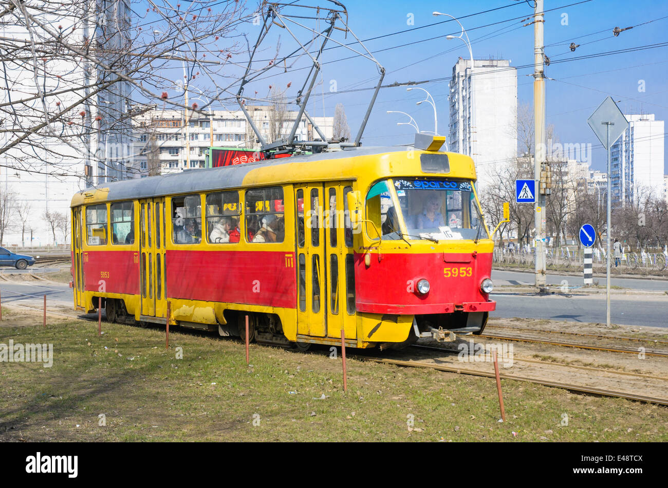 Eine gelbe und rote Straßenbahn in der Timoshemko-Boulevard. Menschen überqueren der Straßenbahnschienen für die Straßenbahn Nummer 16 in Kiew Obolon Viertel Stockfoto