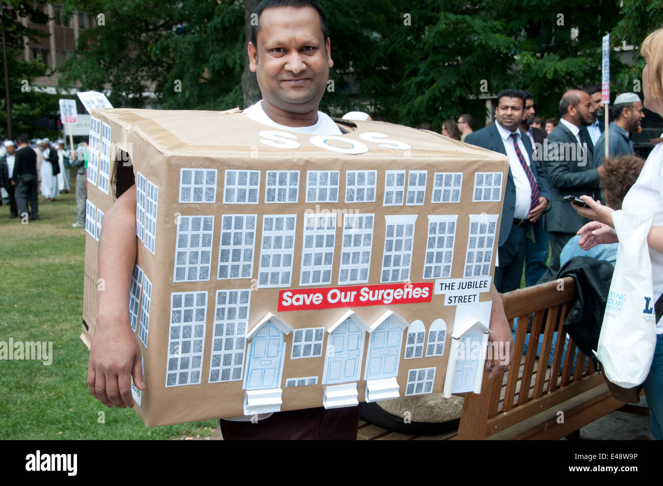 Kundgebung gegen geplante Kürzungen der NHS Arztpraxen. Ein Mann trägt eine dekorierte Box um Operation Jubilee Street vertreten. Stockfoto