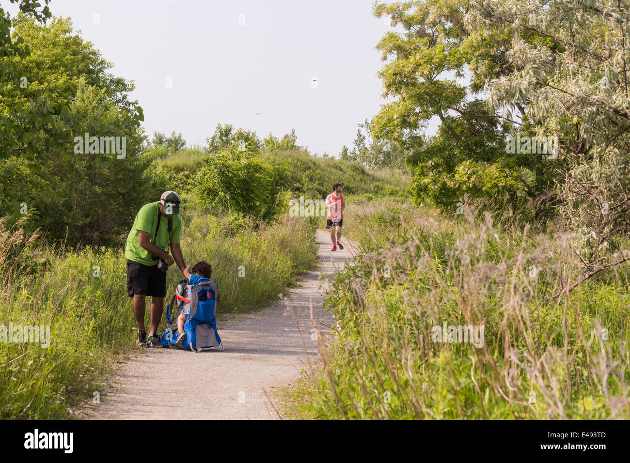Vater mit kleinen Sohn in einem Rucksack sitzt auf dem Boden auf einem Weg, wie ein Jogger, indem kommt Stockfoto
