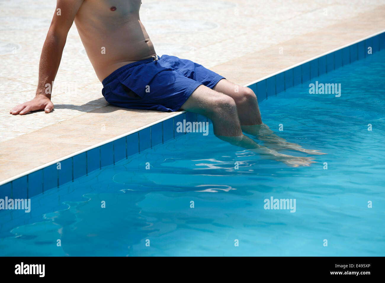 Attraktiver Mann mit blauen Badeanzug sitzt auf dem Rand des Pools Stockfoto