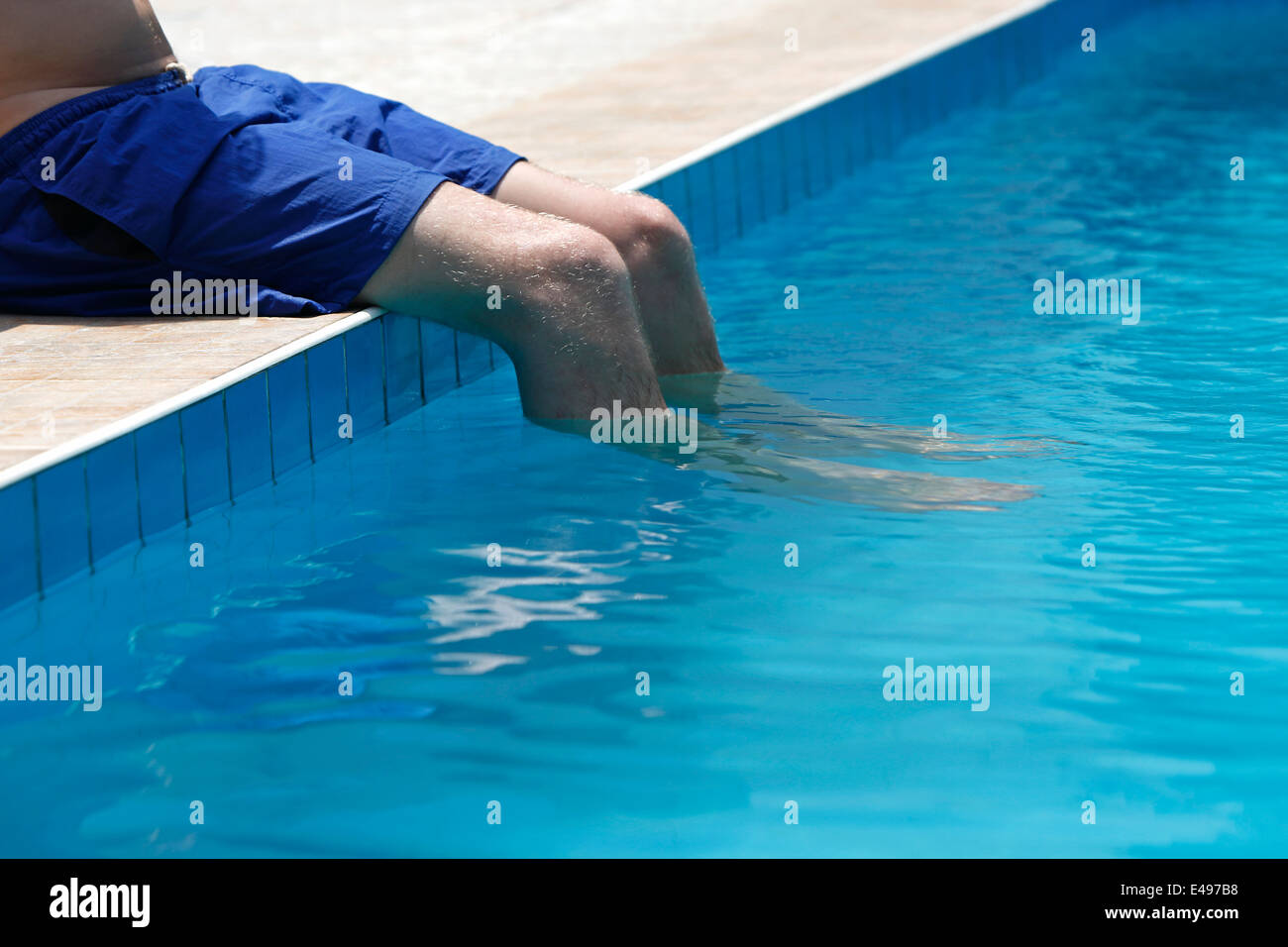 Attraktiver Mann mit blauen Badeanzug sitzt auf dem Rand des Pools Stockfoto
