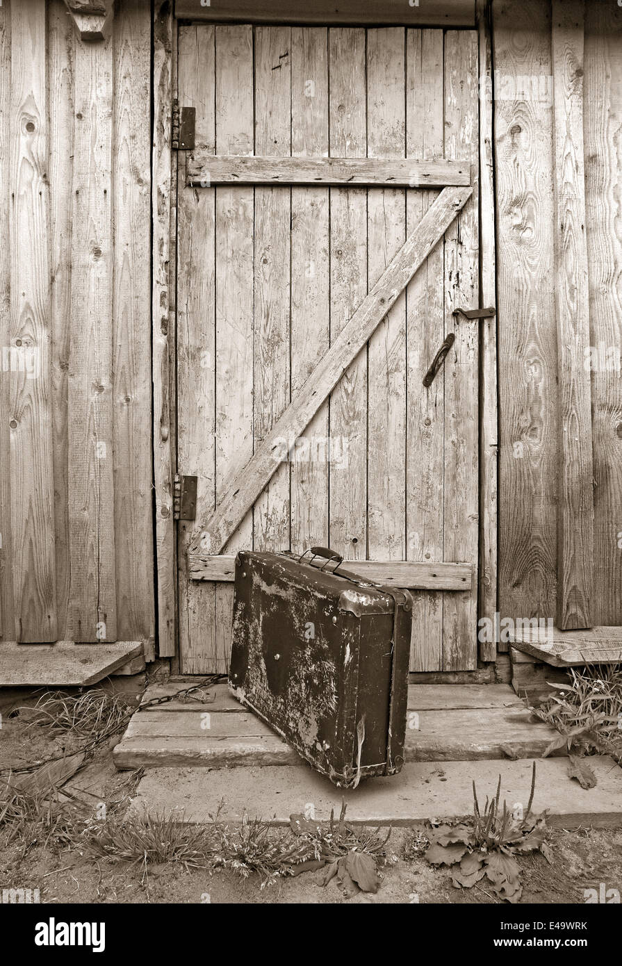 alten Reisetasche in der Nähe von Holztür, sepia Stockfoto