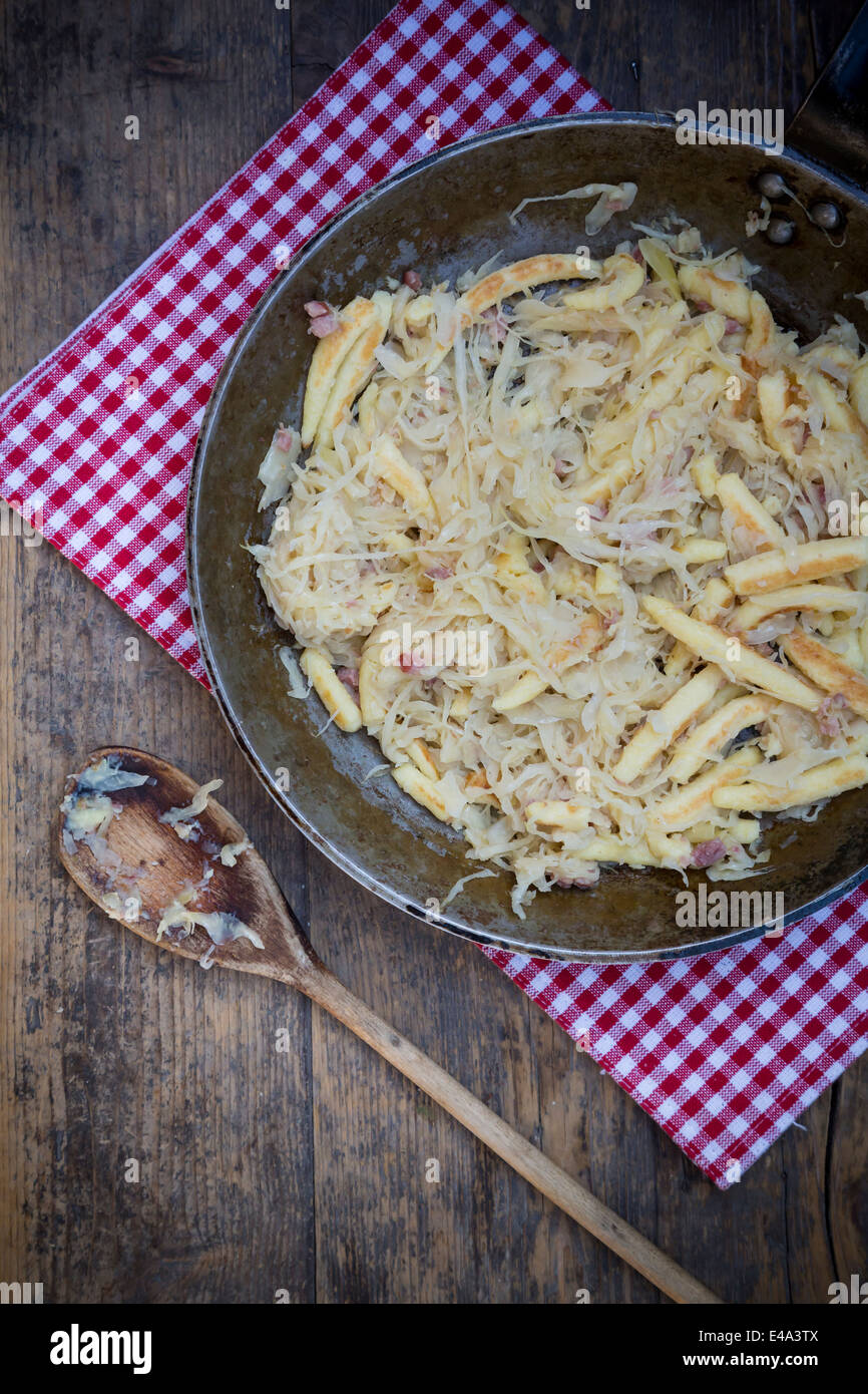 Kochlöffel und Pfanne der fingerförmige Kartoffelknödel mit Sauerkraut und Speck auf Tuch Stockfoto