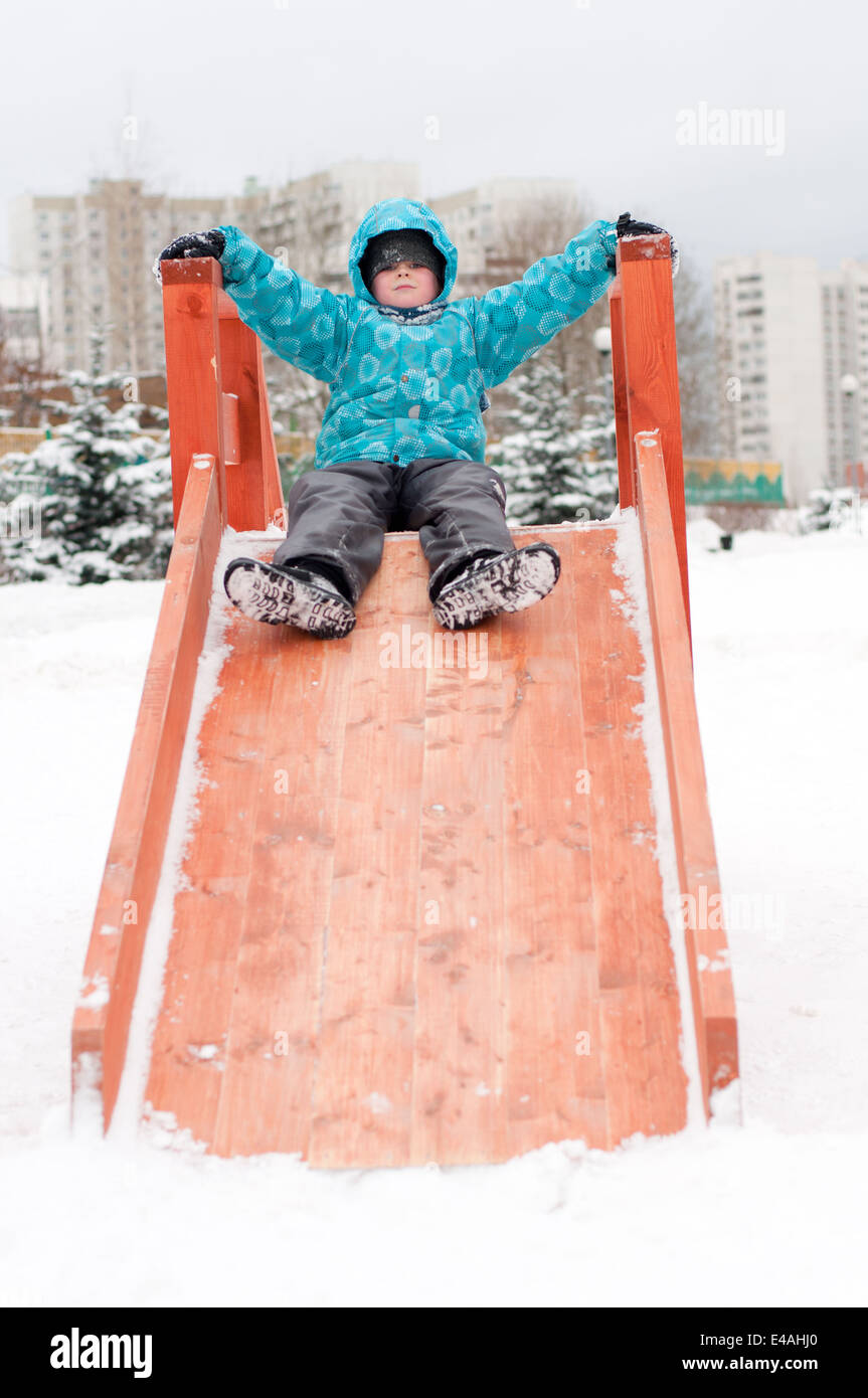 junge Kind ein Kind Hügel Holz Spielsatz Kleidung Winter 8 9 7 Jahr spielen Unterhaltung Freizeit Spaß blaue Jacke Kapuze kalte Frost Moskau Stockfoto