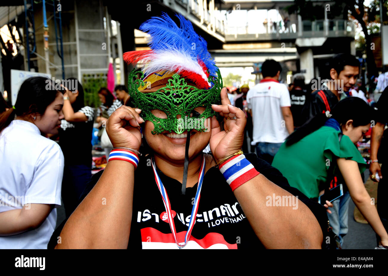 BANGKOK, THAILAND: Frau mit roten, weißen und blauen Federn versucht auf einem reich verzierten Gesichtsmaske auf der Silom Road Stockfoto