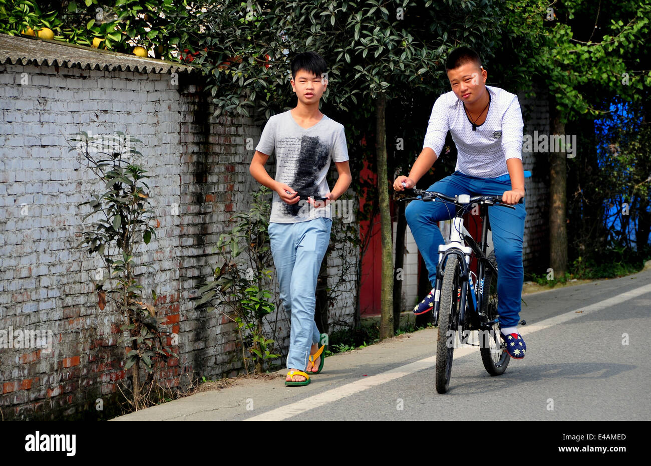 PENGZHOU, CHINA: Zwei junge chinesische Freunde, zu Fuß und per Fahrrad, auf einem Feldweg Stockfoto