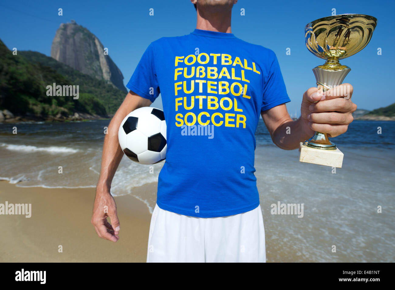 Fußballspieler in Multi Sprache Nachricht T-shirt Holding Trophy und Fußball ball rot Strand Rio de Janeiro Brasilien Stockfoto