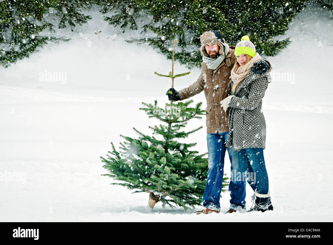 Heterosexuelles Paar steht mit Weihnachtsbaum im tief verschneiten Landschaft, Bayern, Deutschland Stockfoto