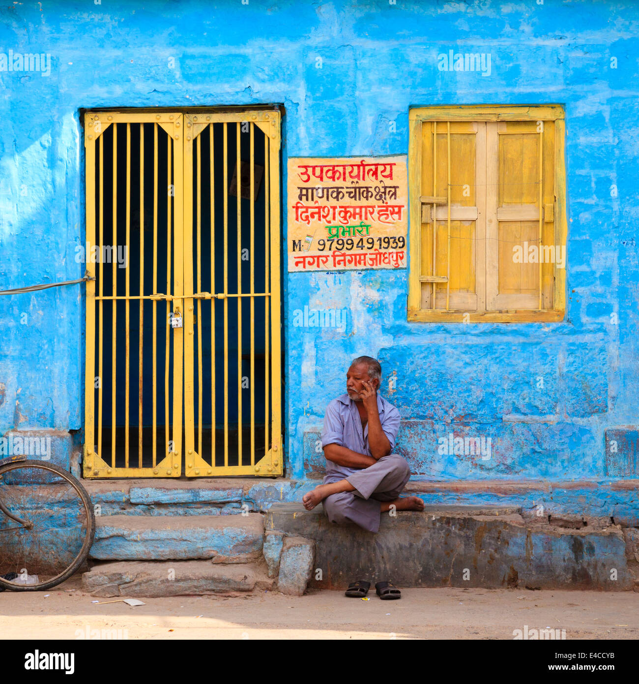 Indischer Mann sitzt draußen bunte Gebäude, Jodhpur, Rajasthan, Indien Stockfoto