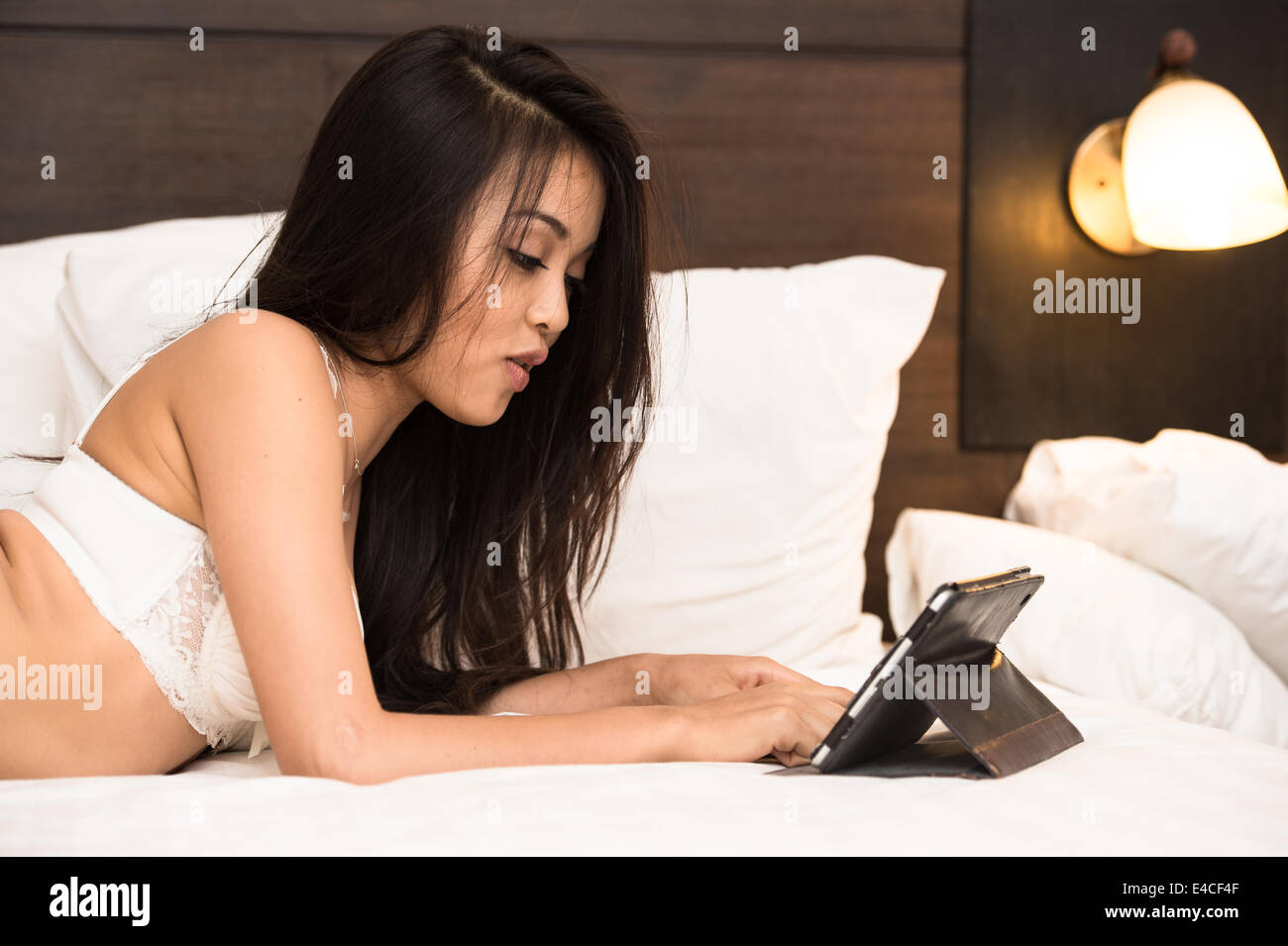 Junge Asiatin tragen Unterwäsche spielen Tablet auf dem Bett im Hotelzimmer Stockfoto