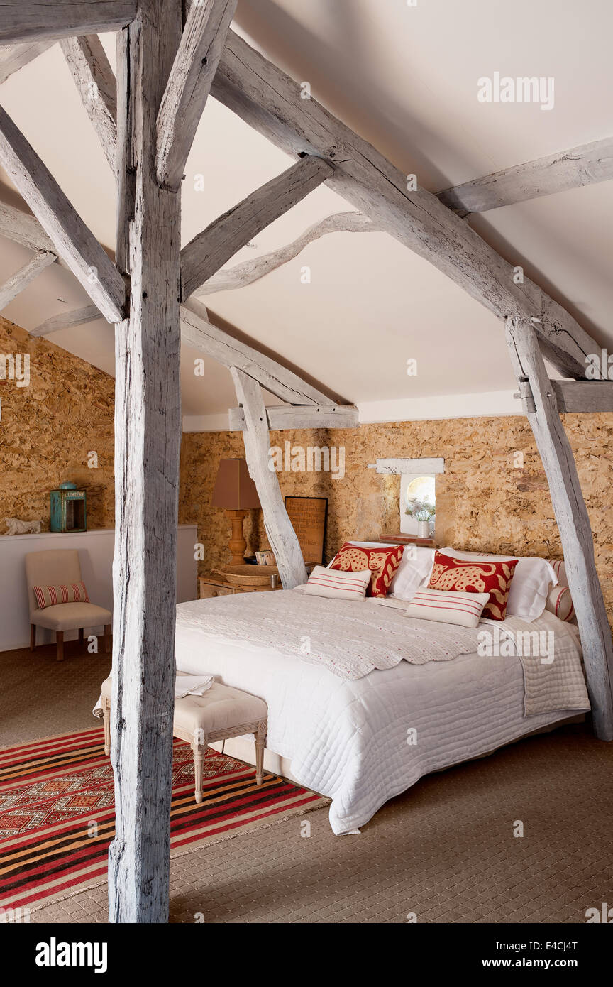 Unverputzte Steinmauern im Dachgeschoss Schlafzimmer mit Holzbalken und marokkanischen Teppich Stockfoto