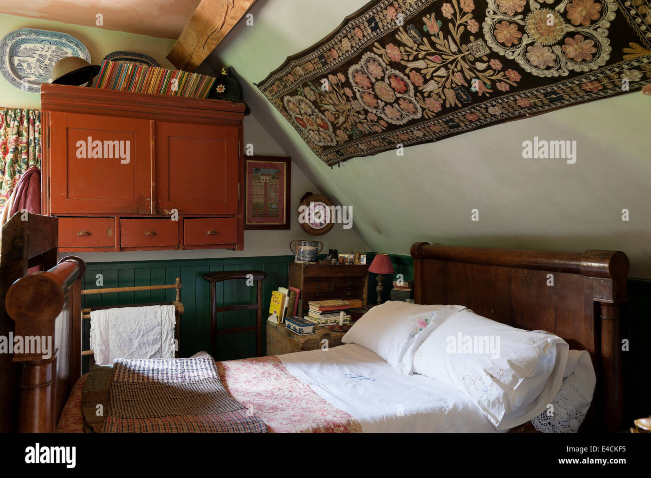 Eine usbekische Textile hängt über ein französisches Reich Bett im Ferienhaus Schlafzimmer mit Tweed Flickenteppich und monogrammiert Leinen Stockfoto
