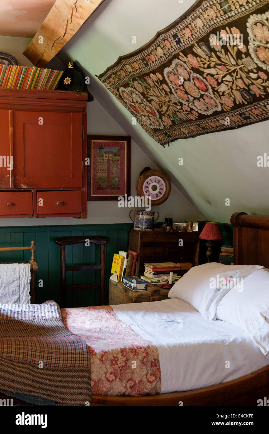 Ein Uzbeki Suzani Textilien hängt über ein französisches Reich Bett im Ferienhaus Schlafzimmer mit Tweed Flickenteppich und monogrammiert Leinen Stockfoto