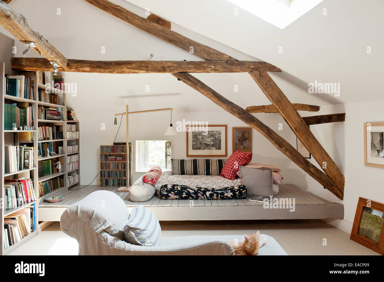 Dachzimmer mit Holzbalken, große Büchergestell, Bodenkissen und Chaiselongue Stockfoto