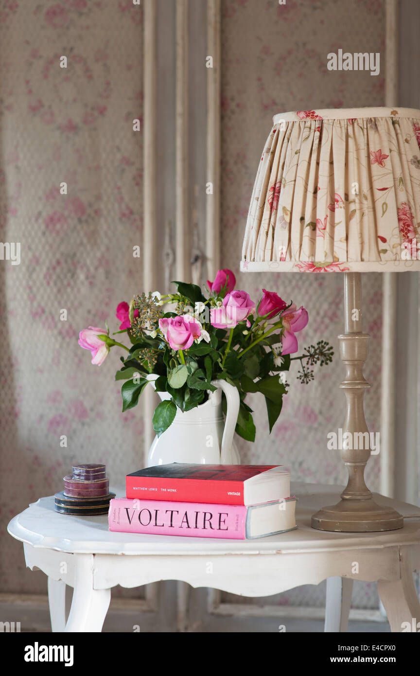 Geraffte Schatten von Kate Forman auf kleinen Holztisch mit Krug mit Rosen und Voltaire Buch Stockfoto