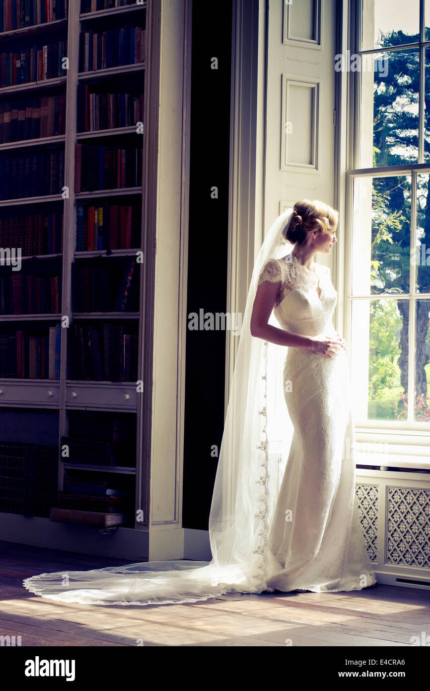 Hochzeitsvorbereitungen, Braut im Hochzeitskleid von Fenster, Dorset, England Stockfoto