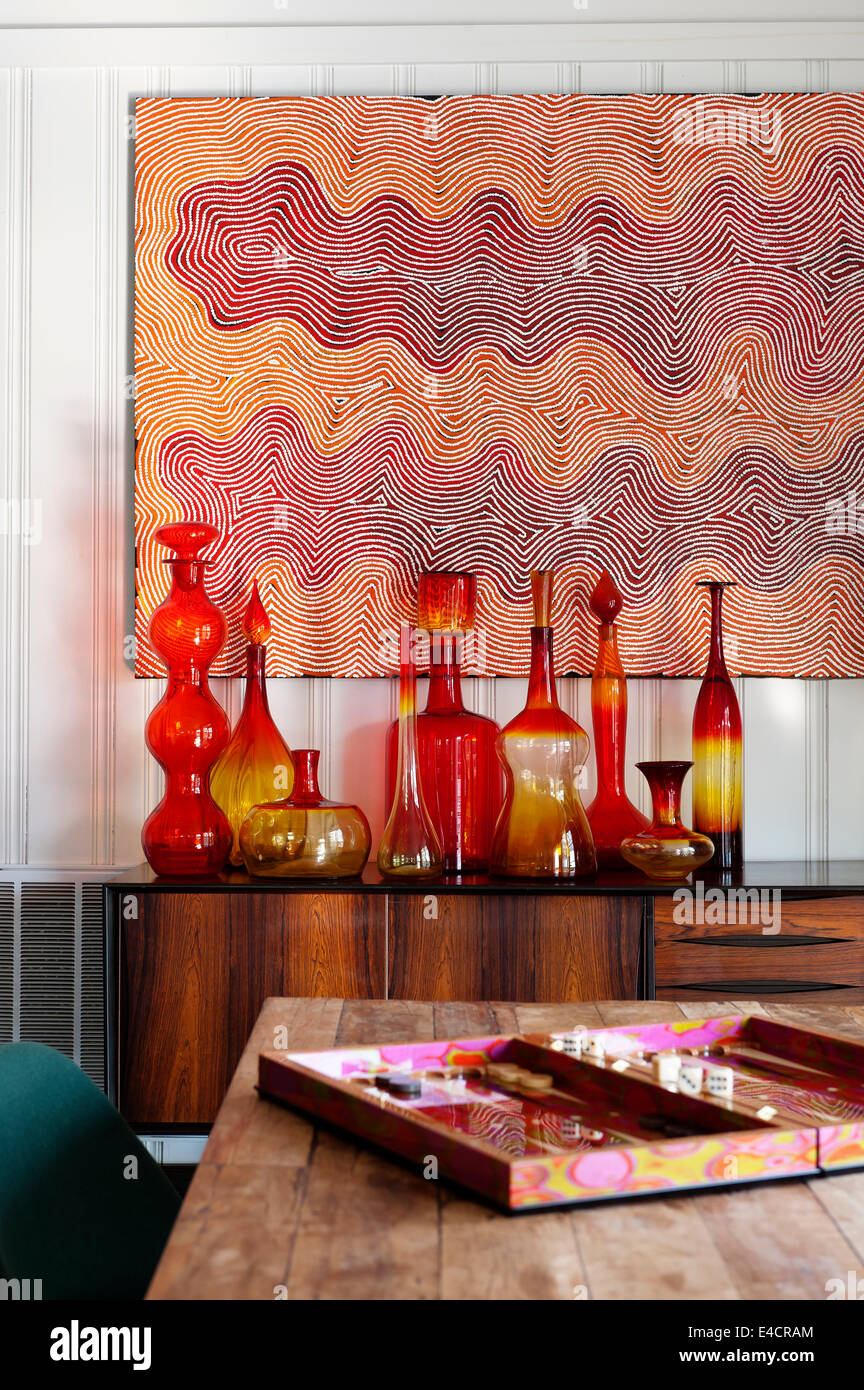 Eine Sammlung von amerikanischen Blenko Glas steht auf einer 50er Jahre Palisander Anrichte. Das Gemälde an der Wand ist von einer australischen Aborigi Stockfoto