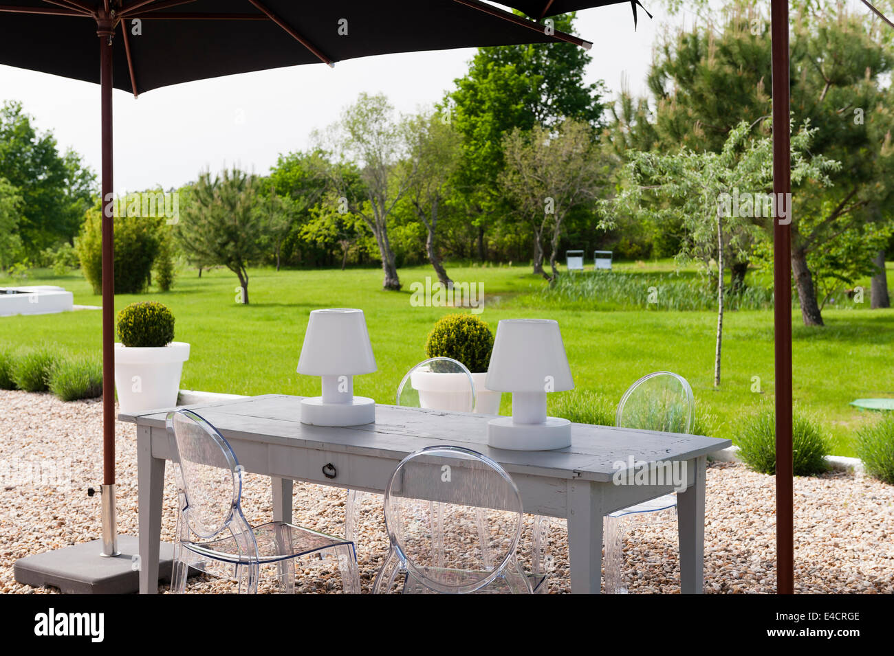 Garten Lichter auf Holztisch mit Philippe Starck Ghost Stühle unter Sonnenschirm im Garten Stockfoto