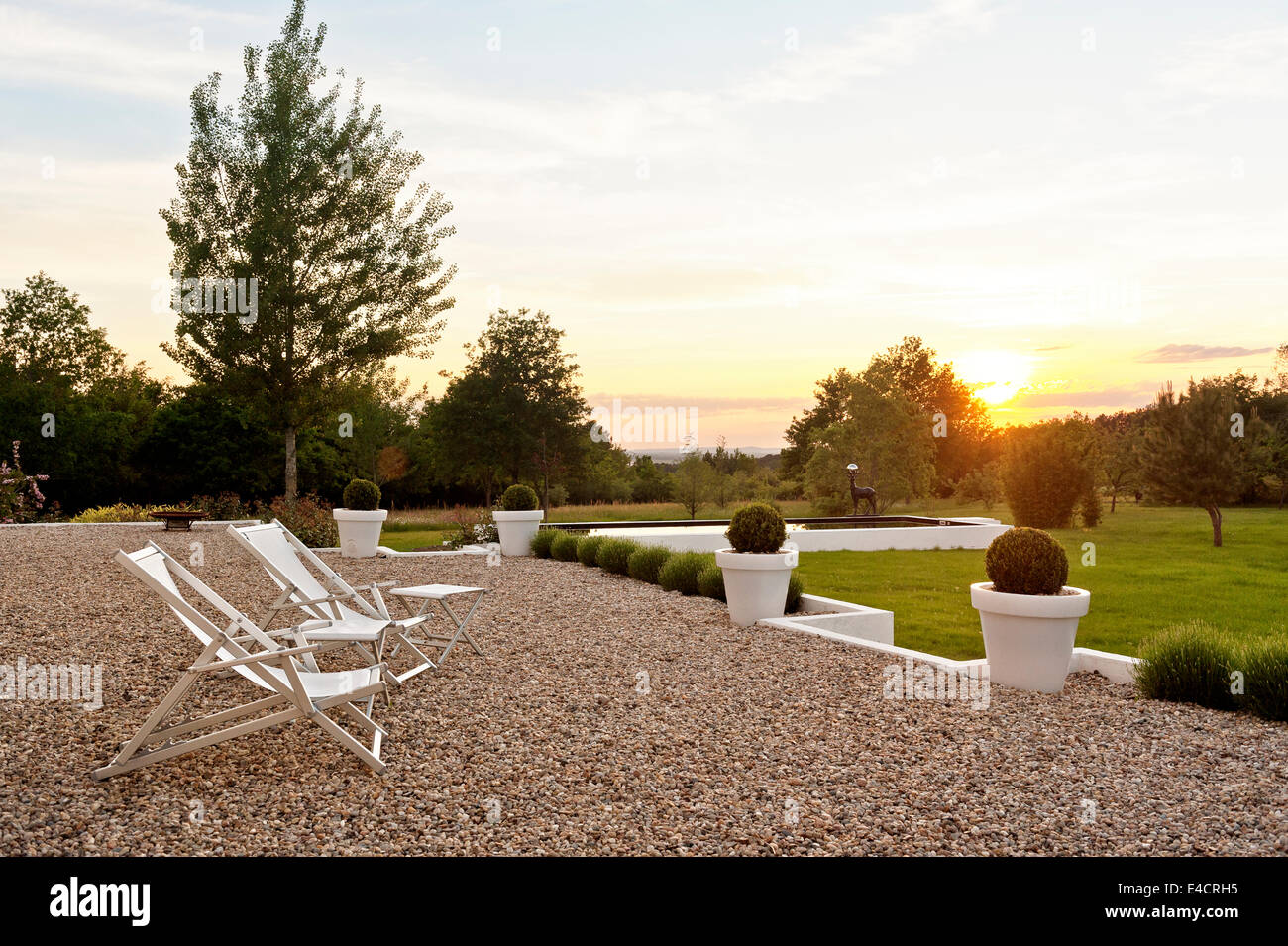 Paar Liegestühle auf Kies Terrasse mit Blick auf den Garten bei Sonnenuntergang Stockfoto