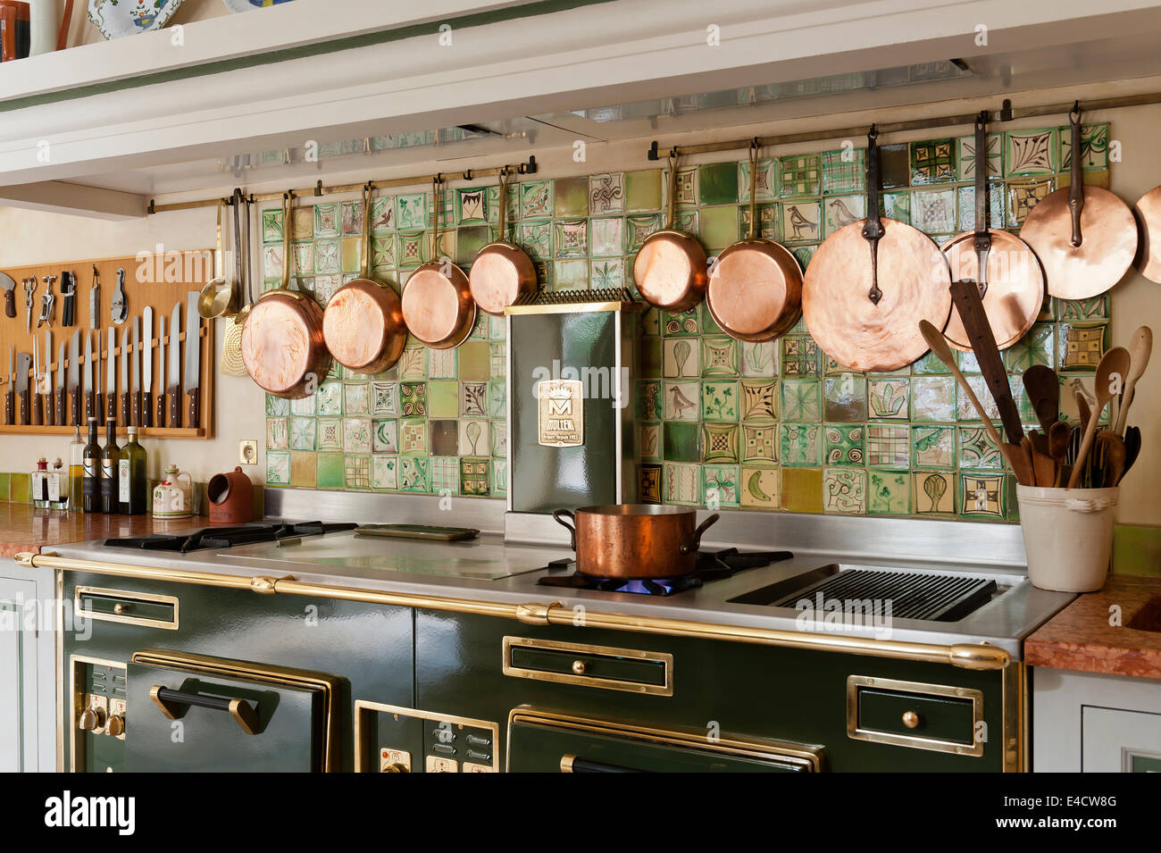 Eine Reihe von Kupfer Pfannen hing über eine semi-professionelle Molteni-Herd in der Küche mit dekorativen Wandfliesen Stockfoto
