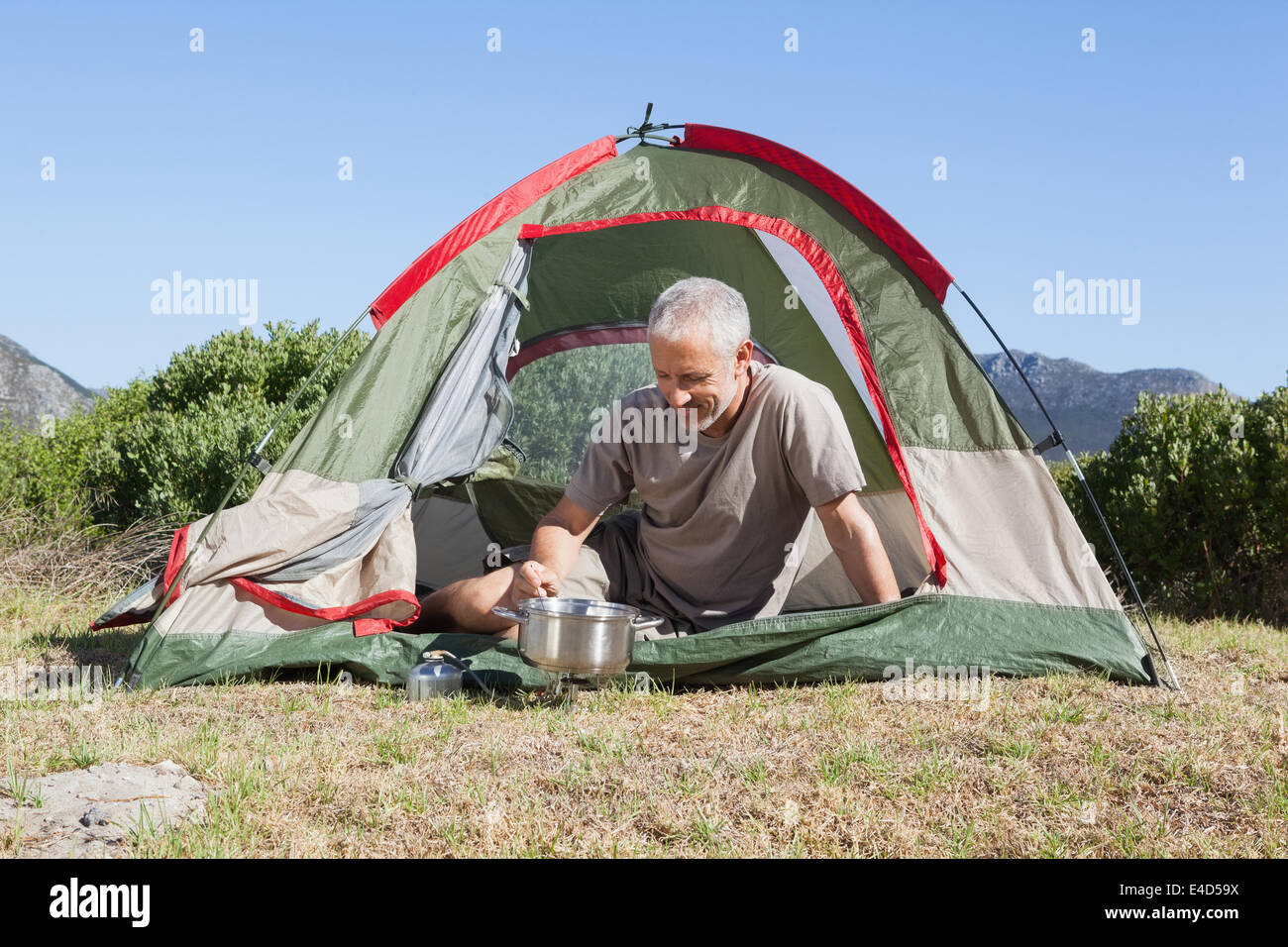 Glücklicher Camper auf Campingkocher außerhalb seines Zeltes Kochen Stockfoto