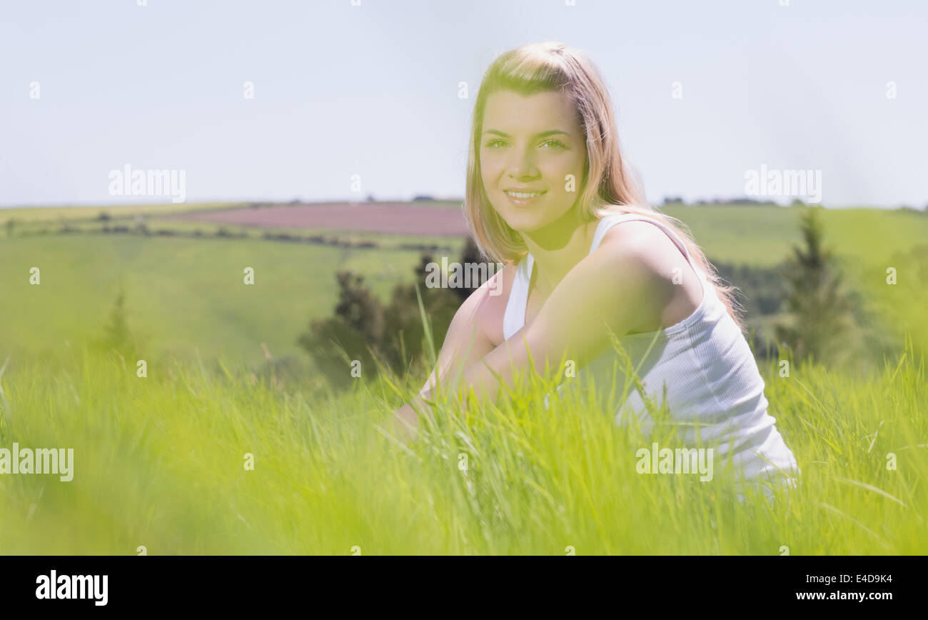 Hübsche Blondine lächelt in die Kamera sitzt auf dem Rasen