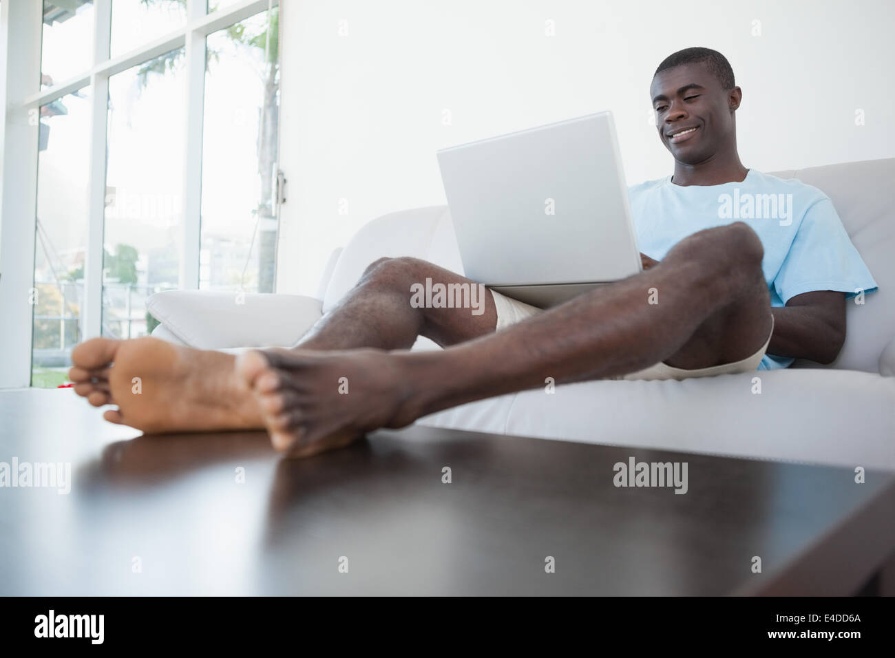 Legerer Mann auf Sofa mit Laptop mit Füßen Stockfoto