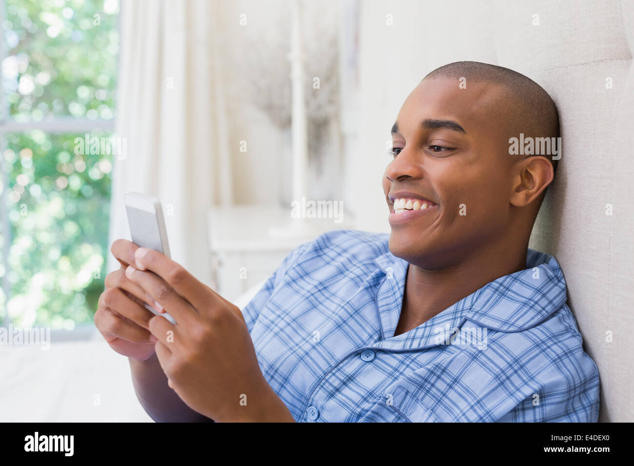 Glücklicher Mann sitzt auf dem Bett und SMS auf Handy Stockfoto