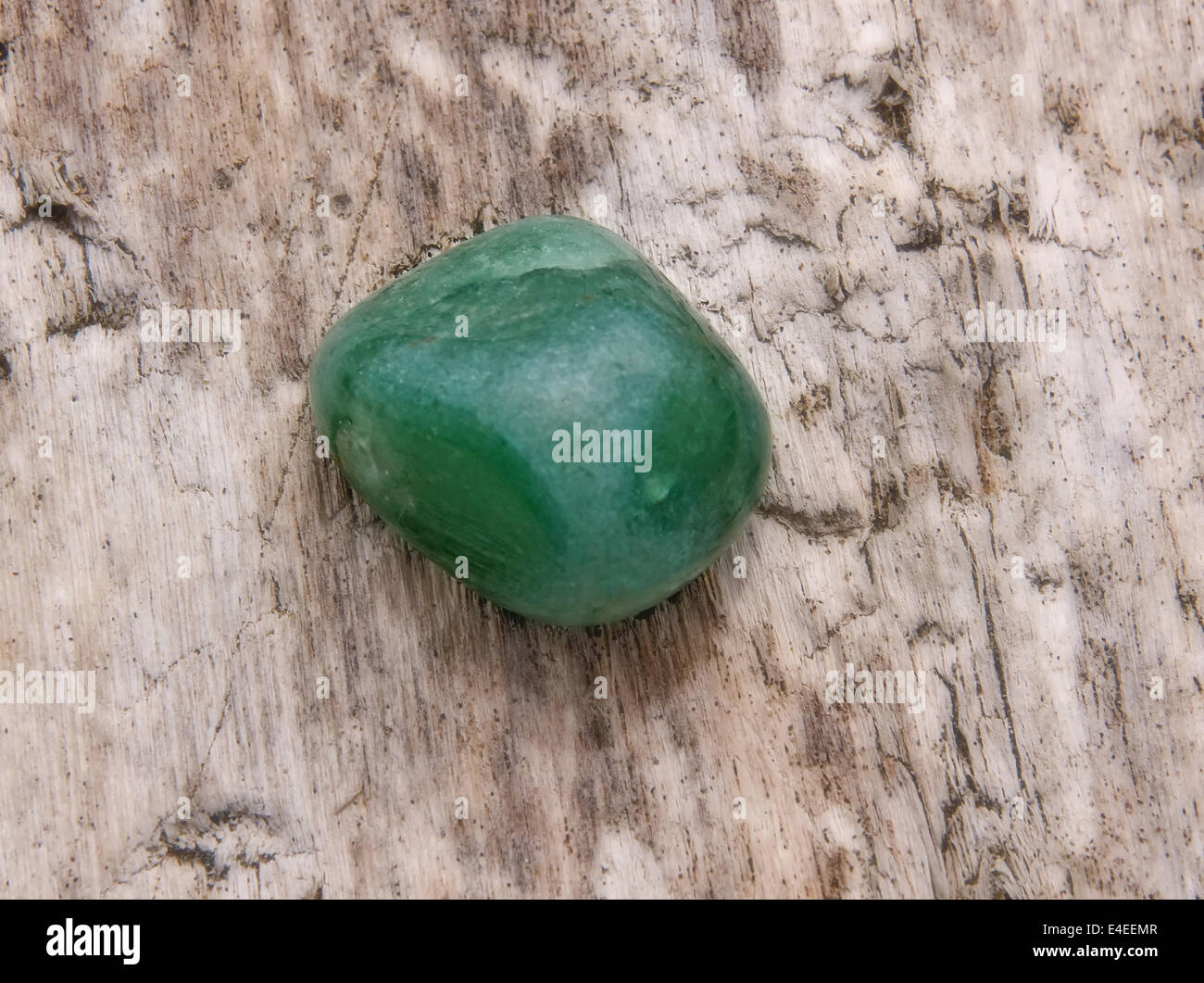 Dies ist eine Nahaufnahme von einer Aventurin grünen Stein sitzt auf einem natürlichen Holz Hintergrund.  Schöne Naturstein grüner Quarz FA Stockfoto
