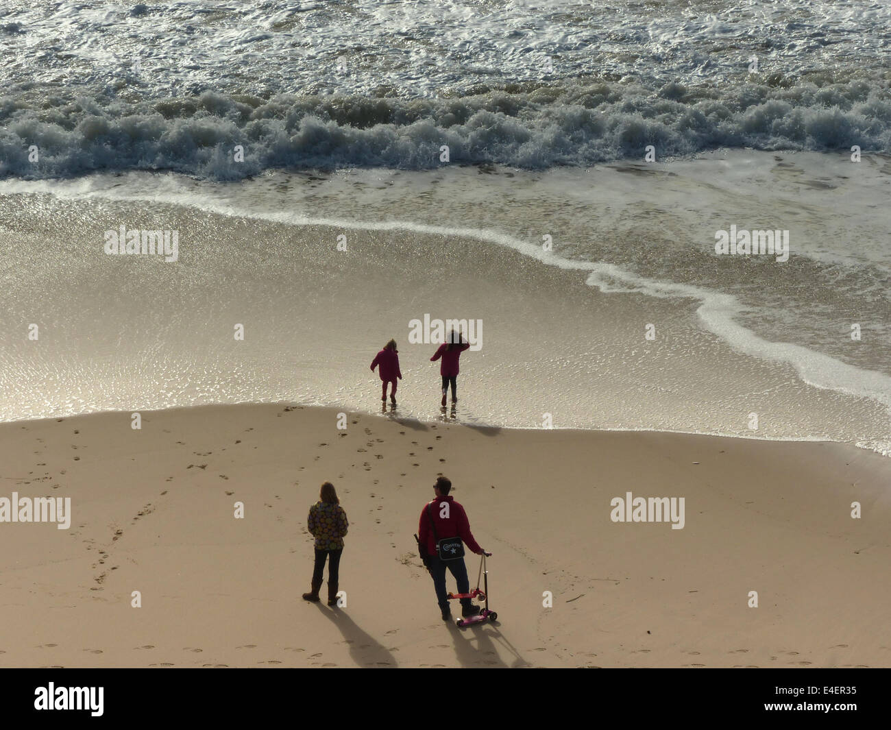 Eine Familie am Meer mit zwei Eltern beobachten zwei Kinder spielen am Wasser Stockfoto
