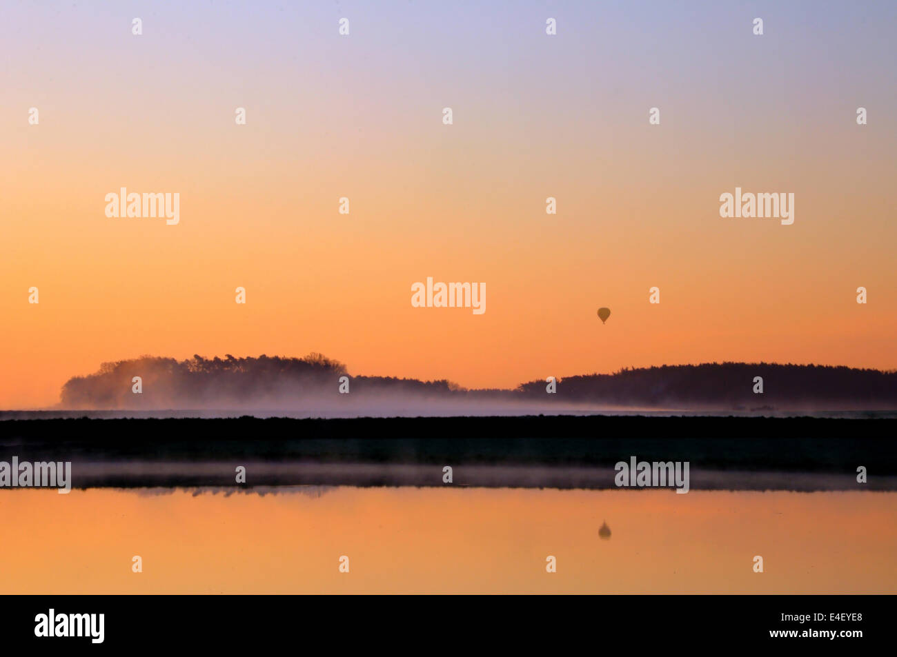 Heißluft-Ballon in den frühen Morgenstunden über einen See in einer ländlichen Landschaft Stockfoto