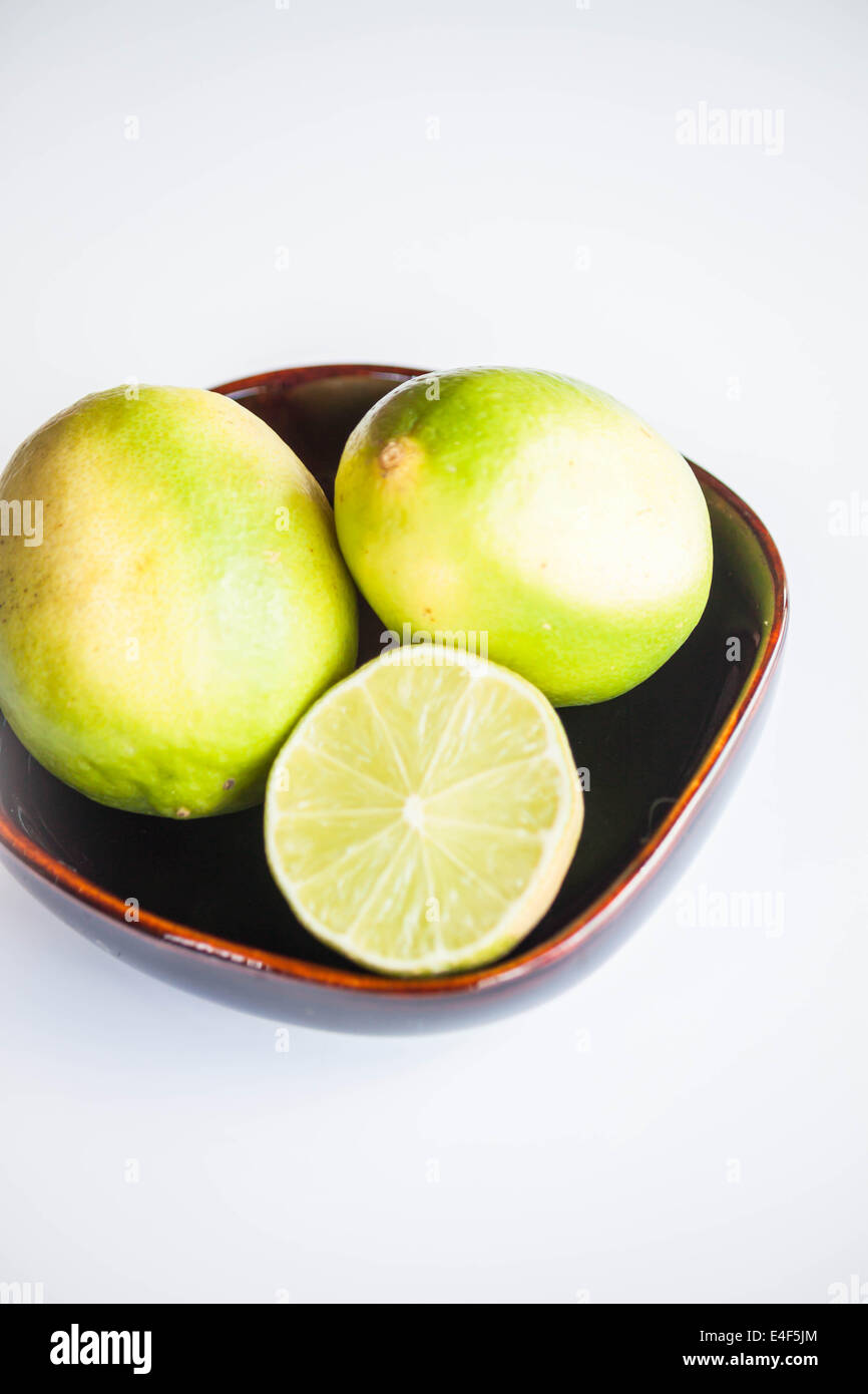 Frische Zitrusfrüchte Limes ganz und in Scheiben schneiden in Keramikschale Stockfoto