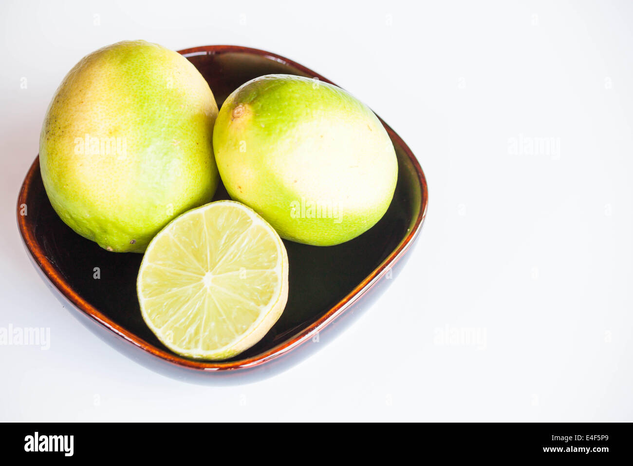 Frische Zitrusfrüchte Limes ganz und in Scheiben schneiden in Schüssel auf weißem Hintergrund Stockfoto