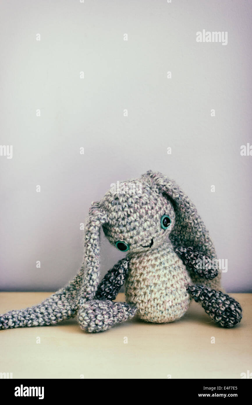 Eine gehäkelte Plüschhase sitzt auf einem Tisch neben einer Wand. Stockfoto