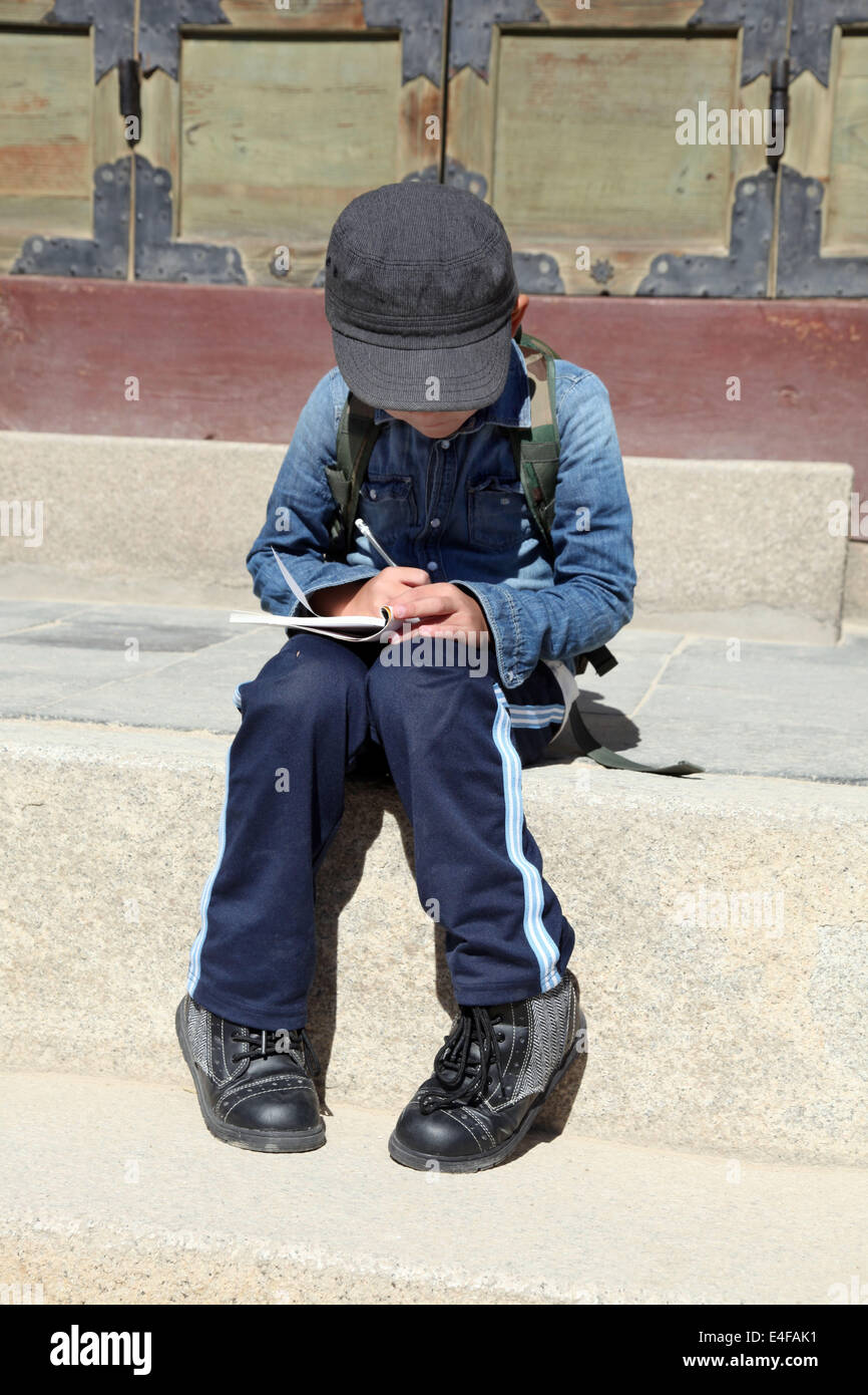 Es ist ein Foto von ein junges Kind oder Kind, das auf eine Steinbank sitzen und ein Buch zu schreiben. Er ist sehr konzentriert Stockfoto