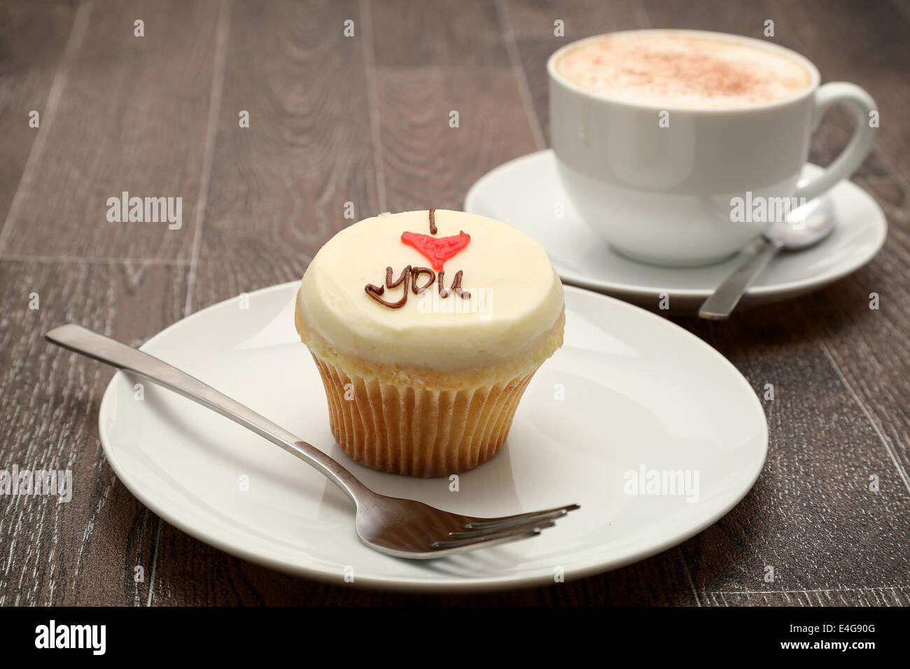 Ein Cupcake garniert mit Buttercreme icing mit der Nachricht "Ich liebe dich", serviert mit einem Cappuccino, Studio gedreht Stockfoto