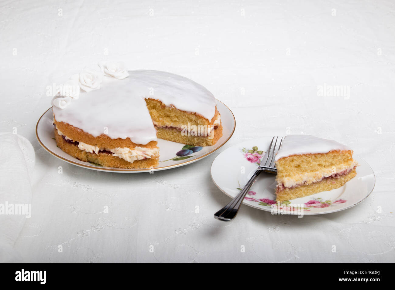 Victoria-Biskuit Eistee in weiß mit handgemachten Rosen auf einem Teller Kuchen auf einem Teller neben (43 von 44) Stockfoto